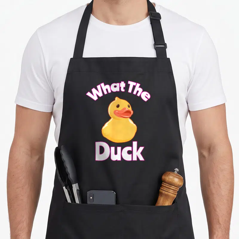 Tablier de cuisine noir avec illustration d'un canard jaune et texte What The Duck en blanc et rose.