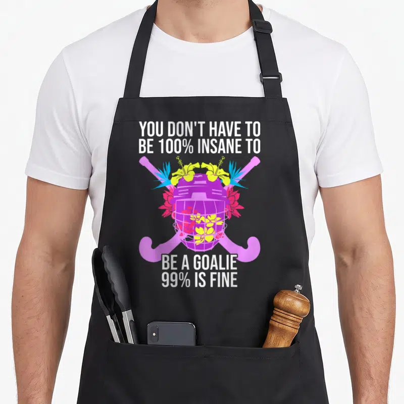Tablier de cuisine noir avec casque de gardier de hockey sur champ violet orné de fleurs jaunes et roses et deux crosses roses croisées.