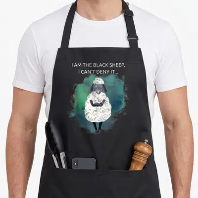Tablier de cuisine noir avec illustration d'un mouton noir sarcastique aux bras croisés et fond aquarelle vert bleuté.