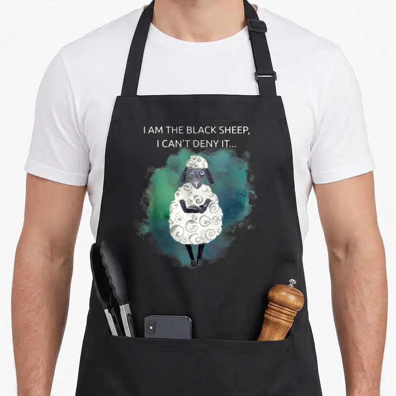 Tablier de cuisine noir avec illustration d'un mouton noir sarcastique aux bras croisés et fond aquarelle vert bleuté.