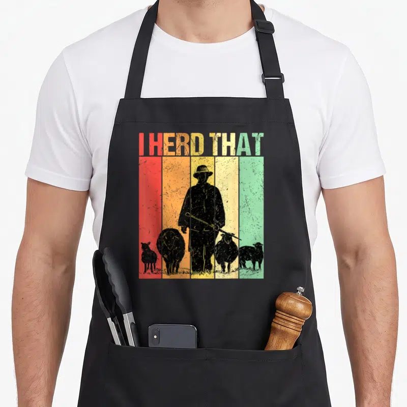 Tablier de cuisine noir avec silhouette berger, moutons et texte I HERD THAT sur bandes colorées vintage.