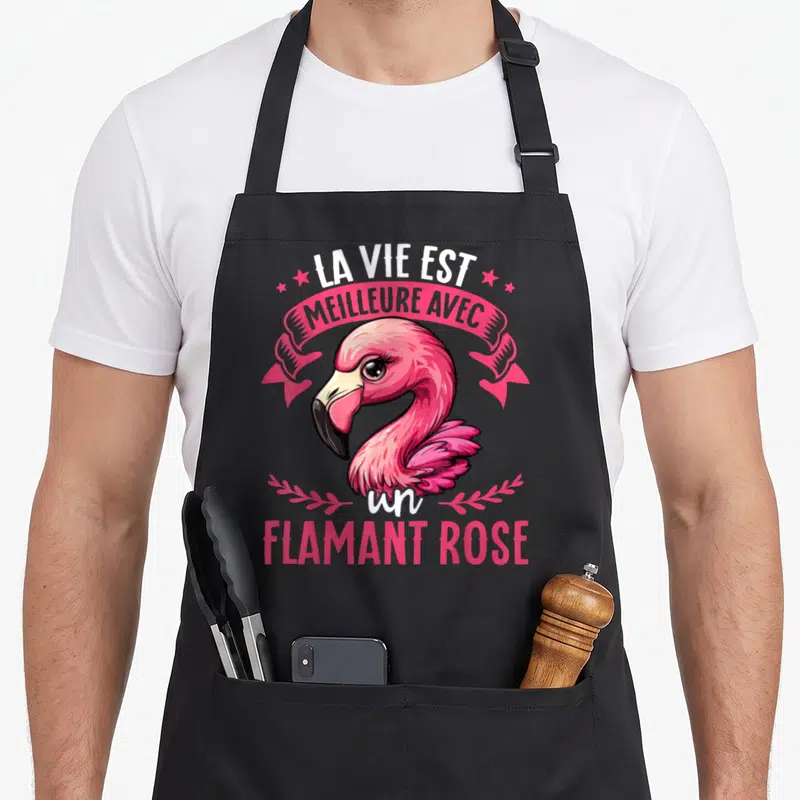 Tablier de cuisine noir avec illustration colorée d'un flamant rose et texte blanc sur banderole rose.