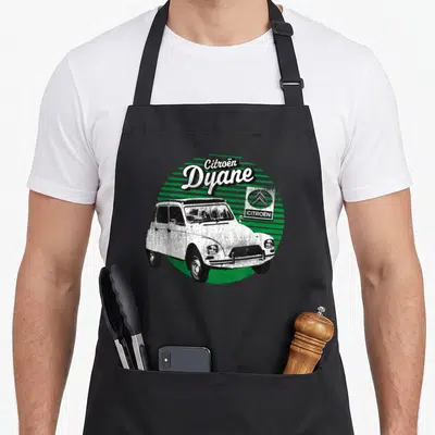 Tablier de cuisine noir avec illustration vintage d'une voiture blanche et texte Citroën Dyane sur fond circulaire vert strié.
