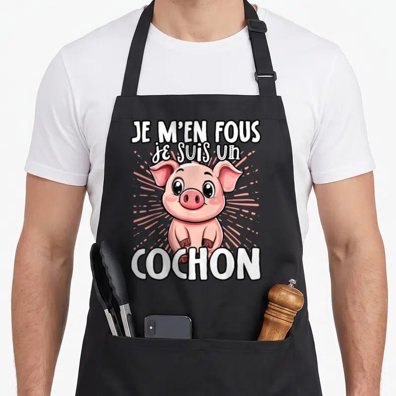 Tablier de cuisine noir avec un dessin de cochon rose et le texte Je m'en fous je suis un cochon en blanc.
