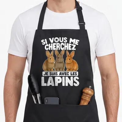 Tablier de cuisine noir avec trois lapins colorés et le texte Si Vous Me Cherchez Je Suis Avec Les Lapins en blanc.