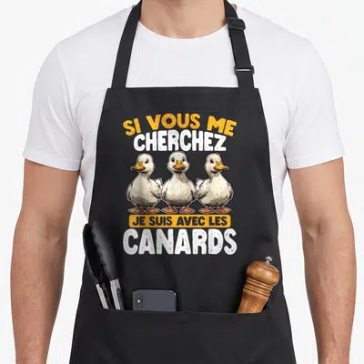 Tablier de cuisine noir avec trois canards blancs et le texte Si Vous Me Cherchez Je Suis Avec Les Canards imprimé en orange et blanc.