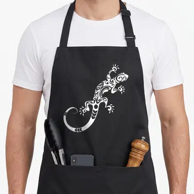 Tablier de cuisine noir avec une illustration blanche d'un lézard au motif tribal et des volutes décoratives sur le corps.