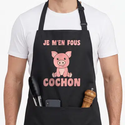 Tablier de cuisine noir avec une illustration rose d'un petit cochon assis et le texte Je m'en fous je suis un cochon en haut et en bas.