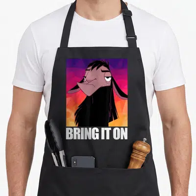Tablier de cuisine noir avec illustration de Kuzco lama sur fond géométrique rose et orange, texte blanc Bring It On en bas.