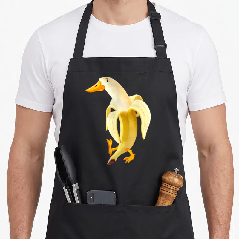 Tablier de cuisine noir avec une illustration d'un canard formé par une banane pelée jaune et orange.