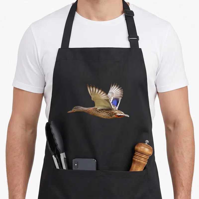 Tablier de cuisine noir avec illustration réaliste d'un canard colvert en plein vol aux ailes déployées.