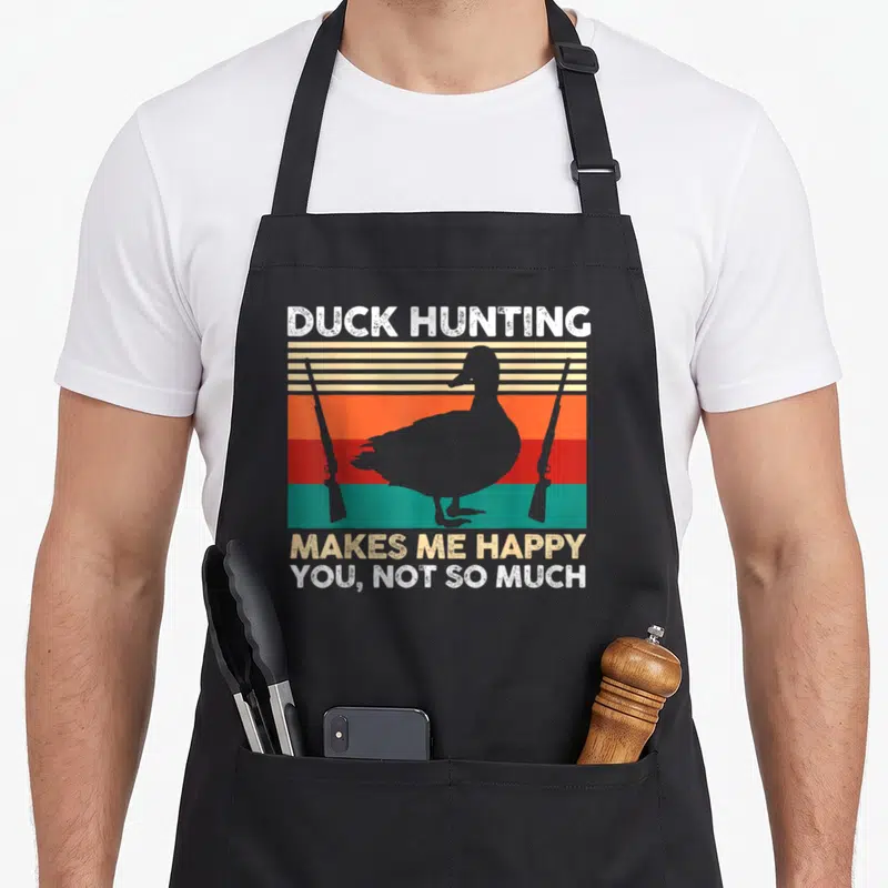 Tablier de cuisine noir avec silhouette de canard, fusils et texte blanc sur fond de bandes colorées vintage.