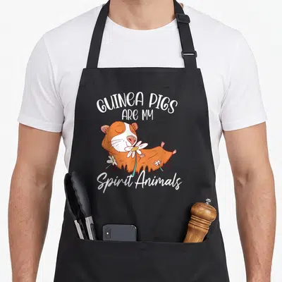 Tablier de cuisine noir avec un cochon d'indie orange dormant entouré de fleurs blanches et le texte guinea pigs are my spirit animals en blanc.