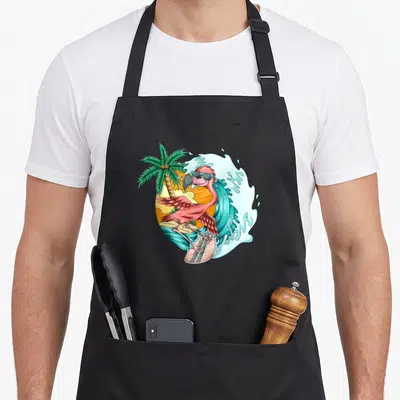 Tablier de cuisine noir avec un flamant rose surfeur portant des lunettes de soleil devant une vague et un palmier.