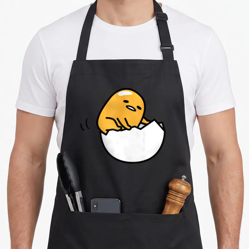 Tablier de cuisine noir avec un jaune dans une coquille blanche cassée et des traits noirs minimalistes.