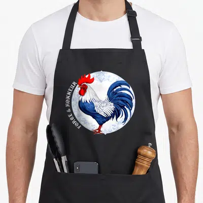Tablier de cuisine noir avec illustration d'un coq bleu et blanc sur un motif de porcelaine blanche.