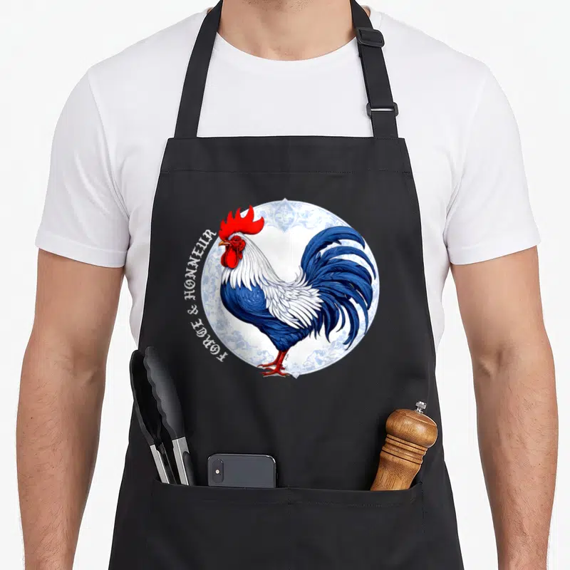 Tablier de cuisine noir avec illustration d'un coq bleu et blanc sur un motif de porcelaine blanche.