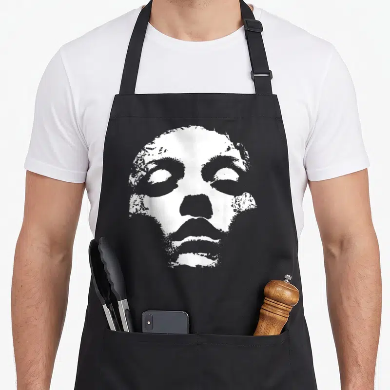 Tablier de cuisine noir avec illustration d'un visage blanc aux yeux fermés et style graphique texturé.