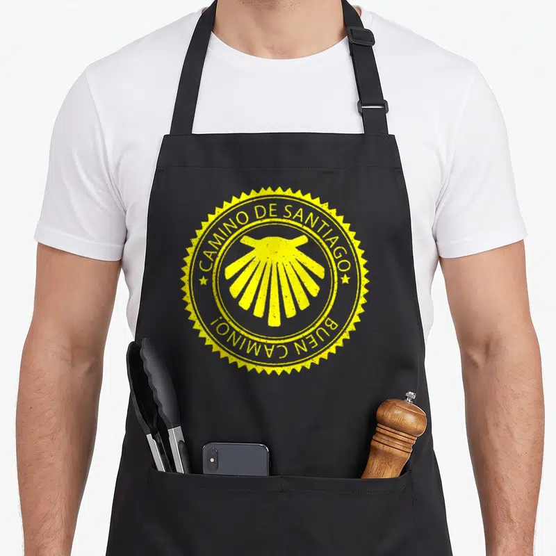 Tablier de cuisine noir avec un logo circulaire jaune représentant une coquille Saint-Jacques et l'inscription Camiño de Santiago Buen Camino.