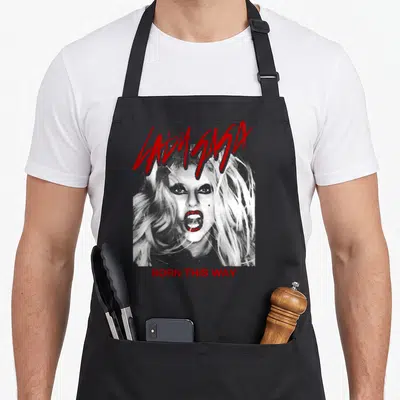 Tablier de cuisine noir avec portrait Lady Gaga et texte Born This Way en rouge vif au style graphique.
