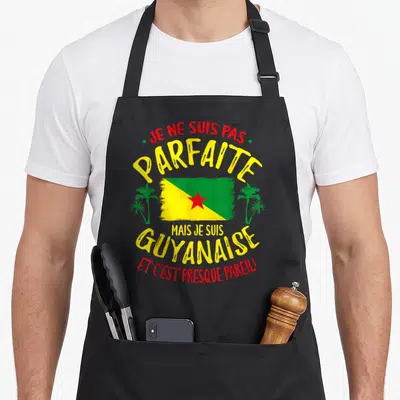 Tablier de cuisine noir avec le drapeau de la Guyane, des palmiers verts et un texte humoristique en jaune et rouge.
