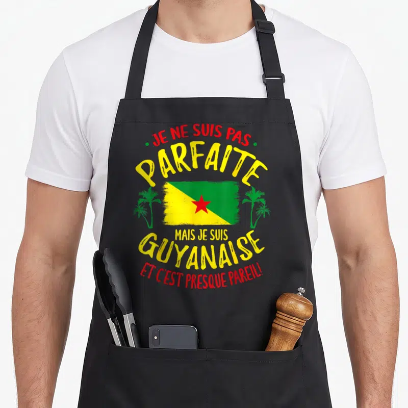 Tablier de cuisine noir avec le drapeau de la Guyane, des palmiers verts et un texte humoristique en jaune et rouge.