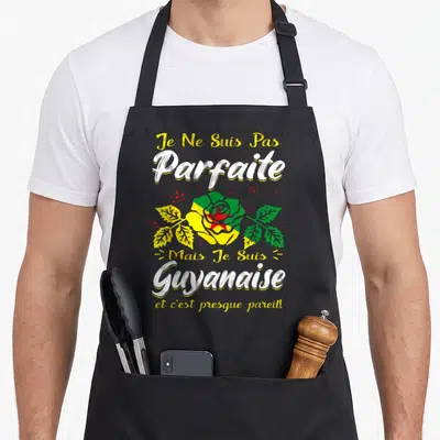 Tablier de cuisine noir avec une rose aux couleurs du drapeau de la Guyane et un texte humoristique en blanc et jaune.