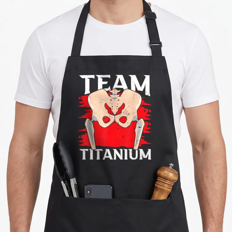 Tablier de cuisine noir avec illustration anatomique de hanche et prothèse en titane sur fond rouge vif.
