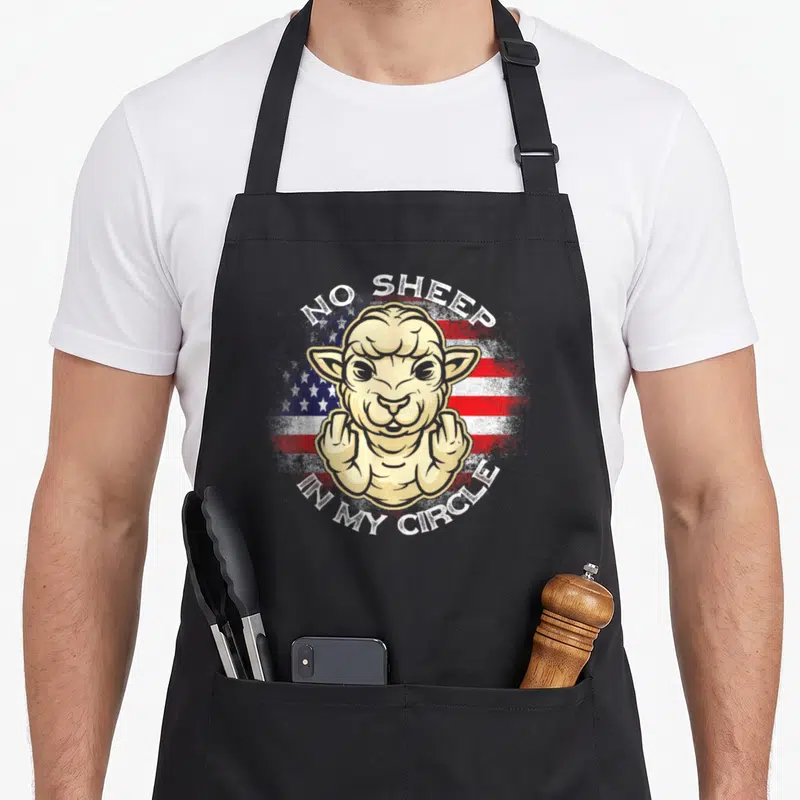 Tablier de cuisine noir avec illustration d'un mouton levant les deux doigts sur fond de drapeau délavé.