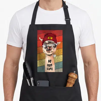 Tablier de cuisine noir avec illustration d'un lama portant des lunettes blanches et un bonnet rouge sur fond coloré.