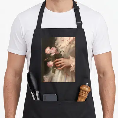 Tablier de cuisine noir avec une illustration romantique de roses roses et une main ornée d'un bijou sur fond sombre.