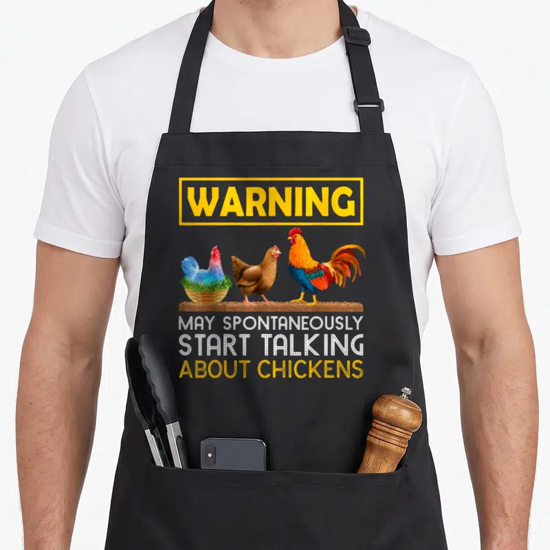 Tablier de cuisine noir avec trois volailles colorées et un message humoristique sur les poules imprimé en jaune et blanc.
