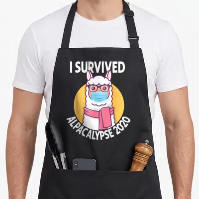 Tablier de cuisine noir avec illustration d'un alpaga portant masque, lunettes et écharpe rose sur fond jaune.