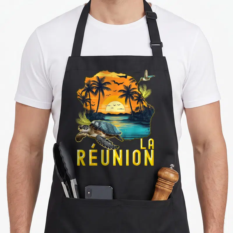 Tablier de cuisine noir avec carte de La Réunion, tortue nageante et texte jaune en bas.