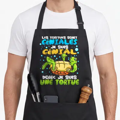 Tablier de cuisine noir avec une tortue verte stylisée et un message humoristique multicolore sur le devant.