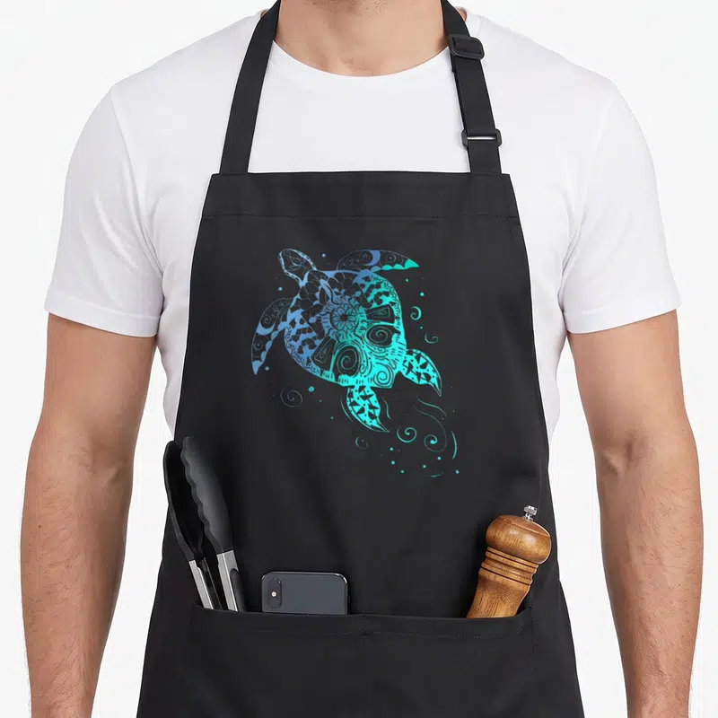 Tablier de cuisine noir avec une tortue de mer stylisée en mandala bleu turquoise et des motifs de plongée sous-marine.