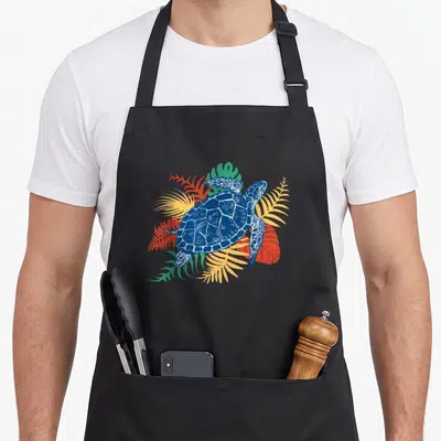 Tablier de cuisine noir avec illustration d'une tortue de mer bleue et de feuilles tropicales multicolores.