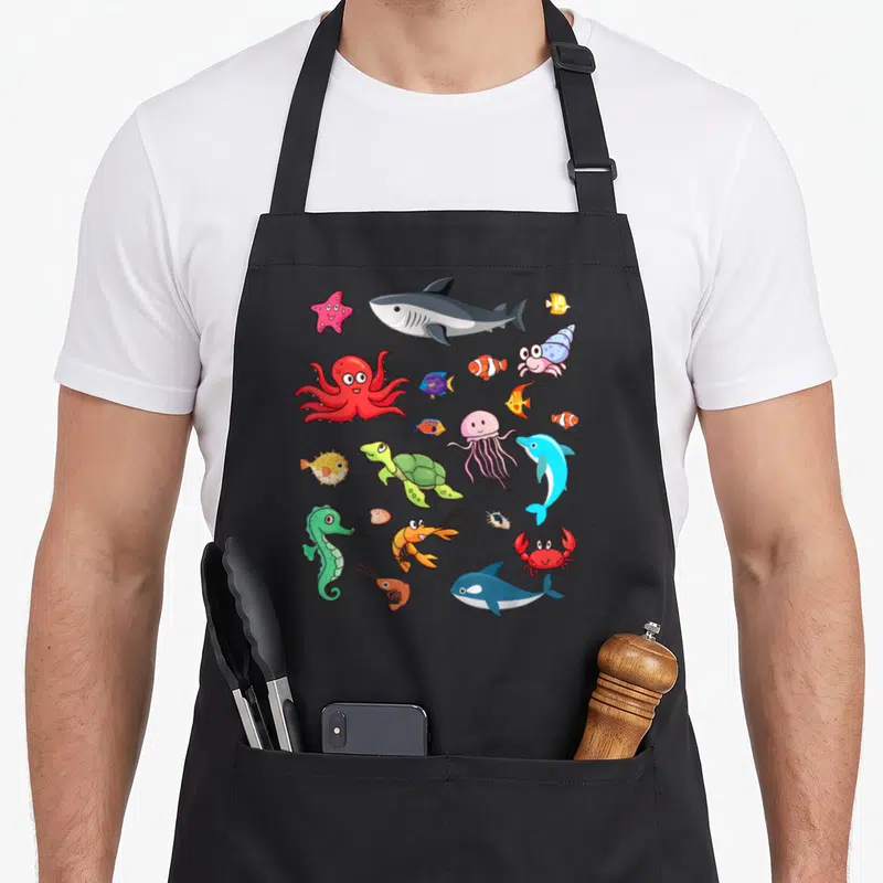 Tablier de cuisine noir avec un poisson clown, un octopus rouge, un shark et divers animaux marins colorés et mignons imprimés au centre.