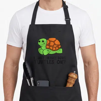 Tablier de cuisine noir avec une tortue verte souriante et le texte I just really love turtles, ok imprimé en noir.