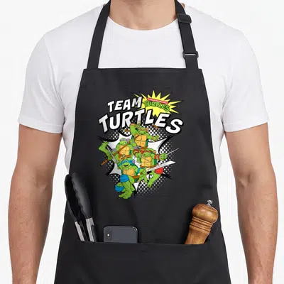Tablier de cuisine noir avec illustration colorée des quatre tortues ninjas en pleine action sous le texte Team Turtles.