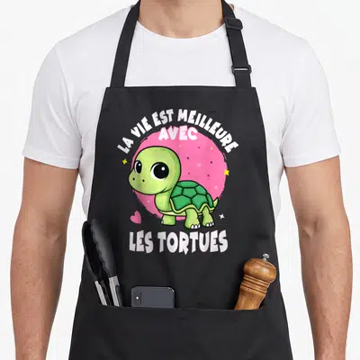 Tablier de cuisine noir avec une tortue verte mignonne et le texte La vie est meilleure avec les tortues sur fond rose.
