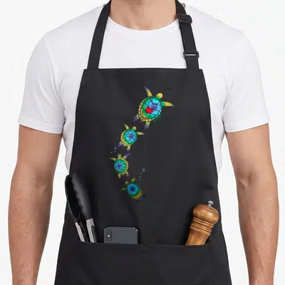 Tablier de cuisine noir avec quatre tortues marines colorées en diagonale et un cœur rouge sur la carapace du dessus.