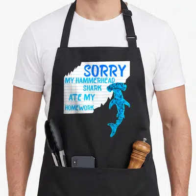 Tablier de cuisine noir avec une illustration de papier écolier et un requin marteau bleu imprimé au centre.