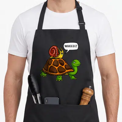 Tablier de cuisine noir avec illustration d'un escargot rouge sur le dos d'une tortue verte et d'une bulle de dialogue.