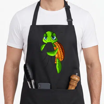 Tablier de cuisine noir avec une tortue verte cartoon aux yeux bleus tenant une serviette grise dans ses nageoires.