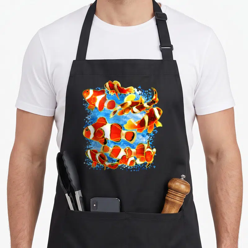 Tablier de cuisine noir avec illustration colorée de plusieurs poissons clowns nageant sur fond bleu aquatique.