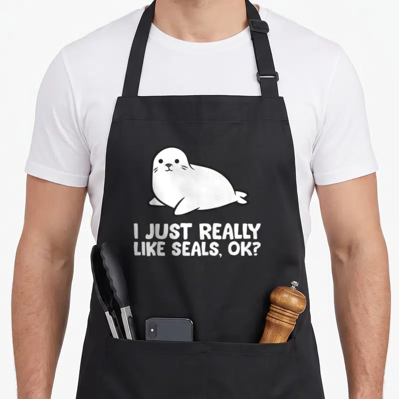 Tablier de cuisine noir avec illustration d'un phoque blanc et texte I JUST REALLY LIKE SEALS, OK?