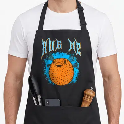 Tablier de cuisine noir avec illustration orange d'un poisson-ballon et texte HUG ME en bleu.