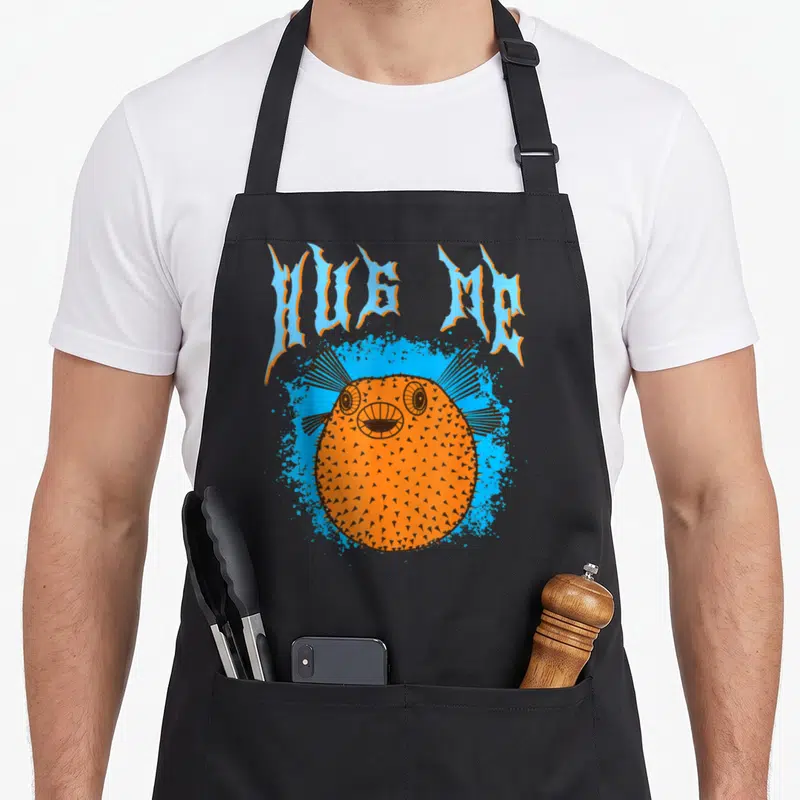 Tablier de cuisine noir avec illustration orange d'un poisson-ballon et texte HUG ME en bleu.