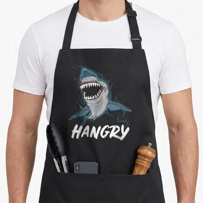 Tablier de cuisine noir avec illustration de requin aux dents visibles et texte hangry en blanc.